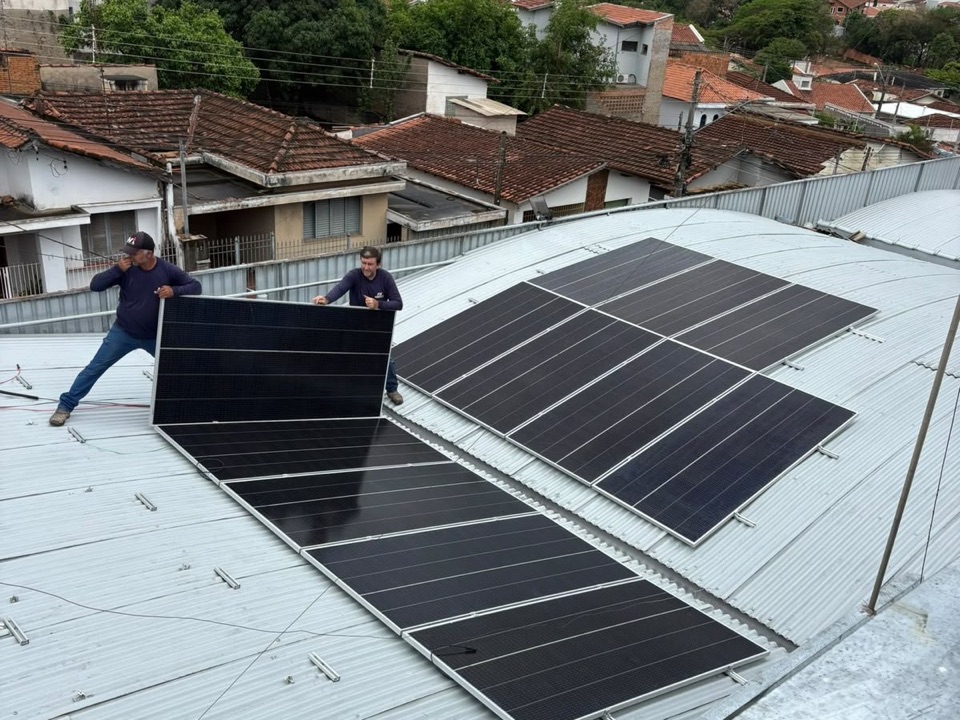 Equipe da MV EnergySol carregando uma placa solar no telhado, com a cidade e a serra ao fundo